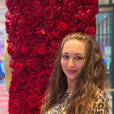 Woman with long hair stands beside a wall covered in red roses.