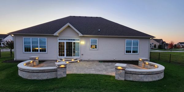 Outdoor living space with Unilock paver patio, seating walls, pillars, steps, Kichler lighting. 