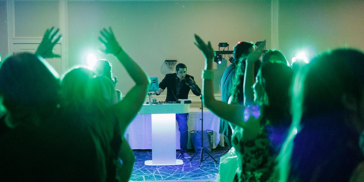 DJ at a party with people dancing and raising their hands.