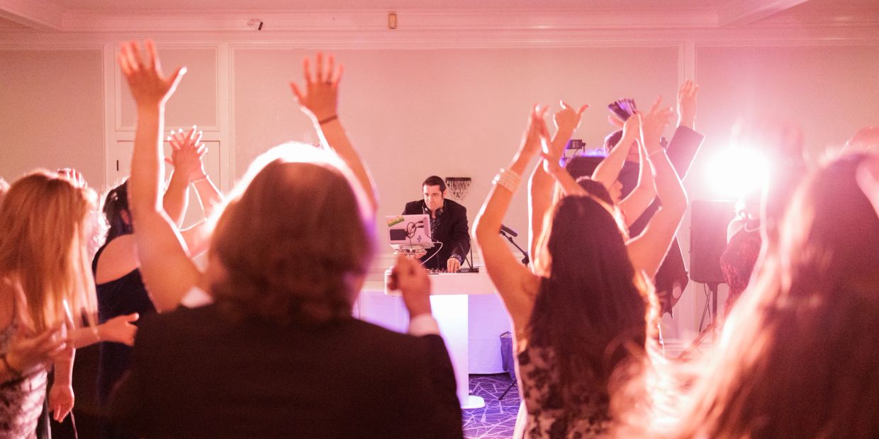 Party guests dancing with DJ in background.