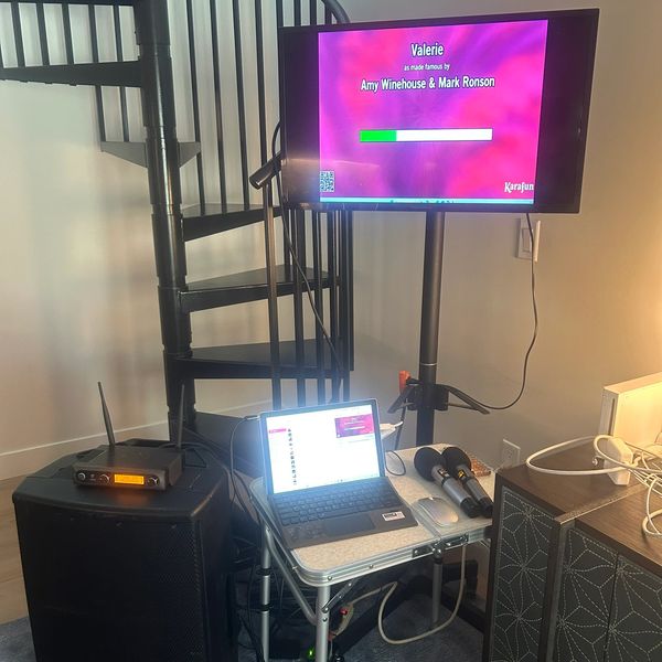 Karaoke setup with microphones, laptop, and TV screen.