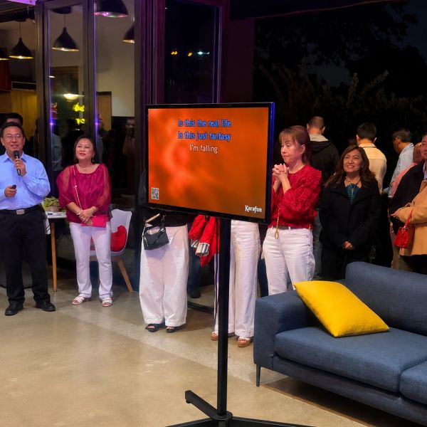 People singing karaoke indoors with a TV screen showing karaoke lyrics.
