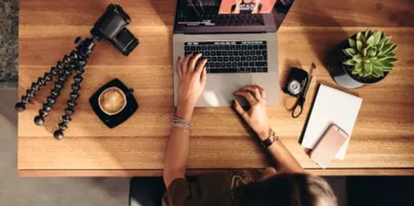 Person working on a laptop at a wooden desk with coffee and camera.
