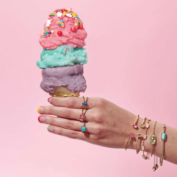 Hand holding a colorful triple-scoop ice cream cone with sprinkles and rainbow decorations.