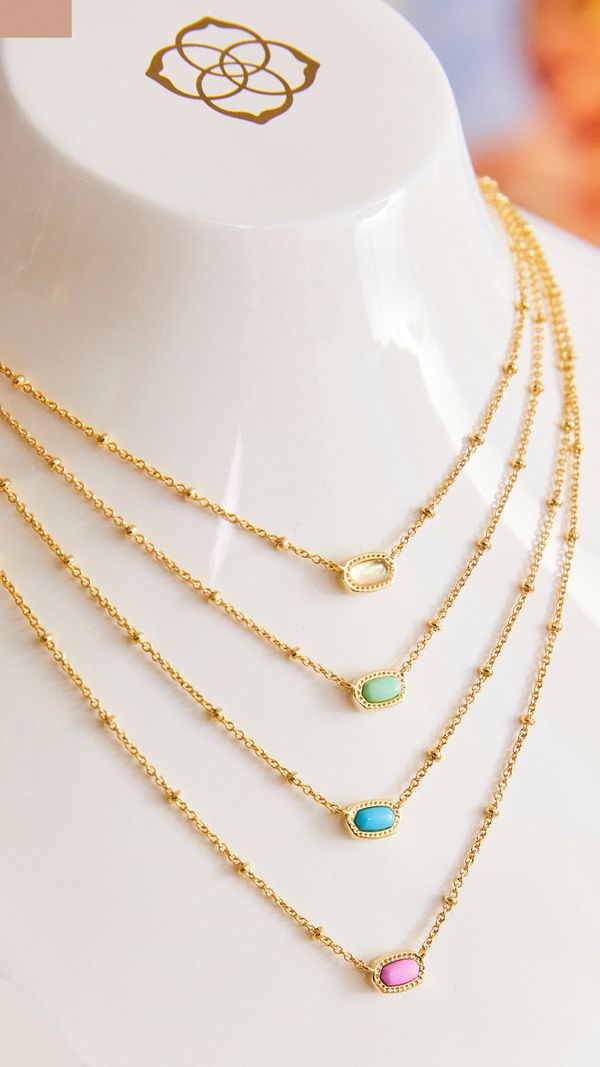 Four delicate gold necklaces with colorful stone pendants displayed on a white stand.