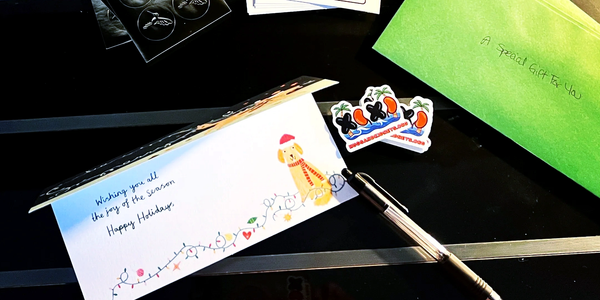 Holiday card, pen, and gifts on a black table.