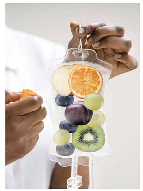 A black provider holding an IV bag filled with various fruits. 