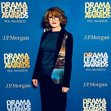 A woman posing at the Drama League Awards event with a blue backdrop.