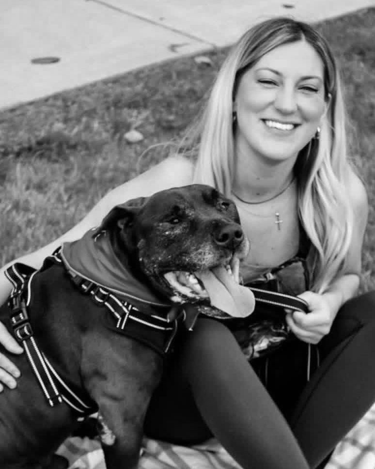 Smiling woman sitting on a blanket with a happy black dog wearing a red bandana.
