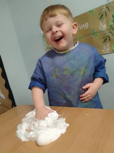 Happy child playing with foam on a table, wearing a paint smock.