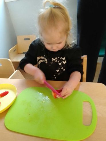 Young child cutting a tomato on a green cutting board.