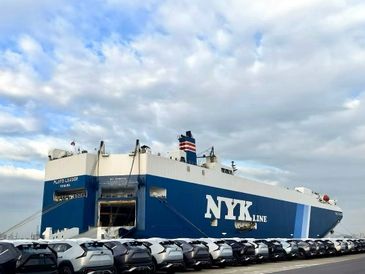 Large NYK Line cargo ship docked with cars lined up in front.