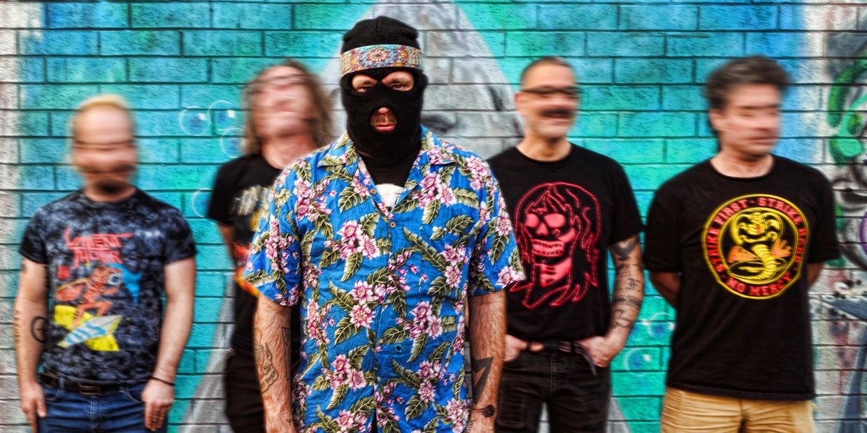 Man wearing a balaclava and floral shirt in front of a brick wall with four blurred men.