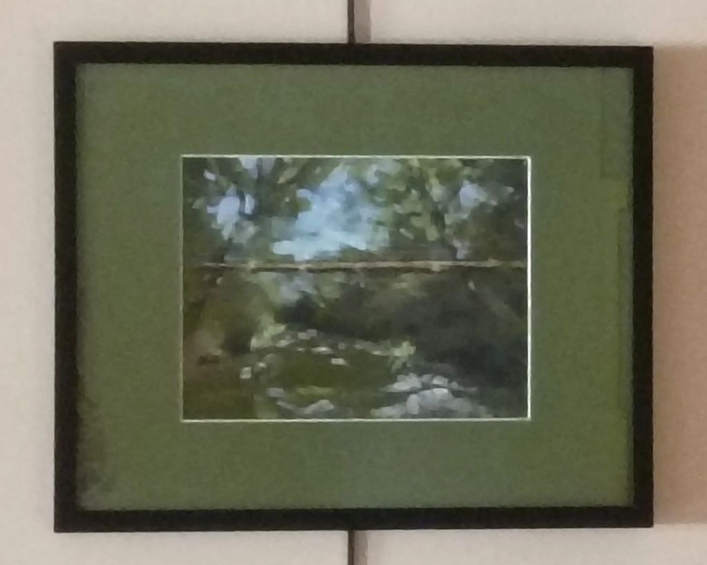 Framed impressionist painting of a serene river scene with trees.