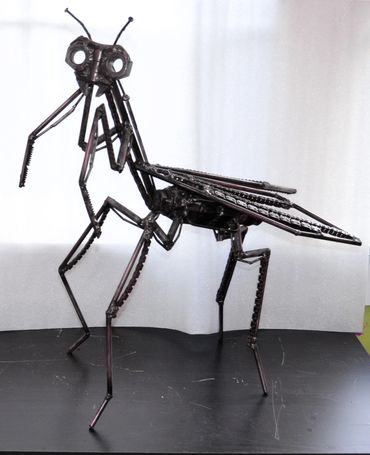 Metal sculpture of a praying mantis made from mechanical parts.