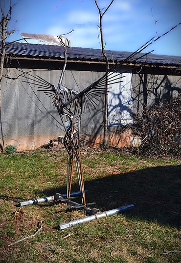 Metal sculpture of a bird with outstretched wings in a yard.