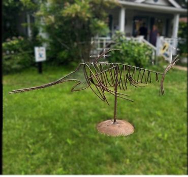 Metal sculpture of a fish with a long snout displayed on a lawn.