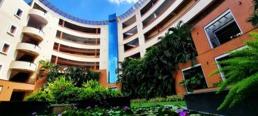 Curved modern building with lush greenery in the courtyard under a blue sky.