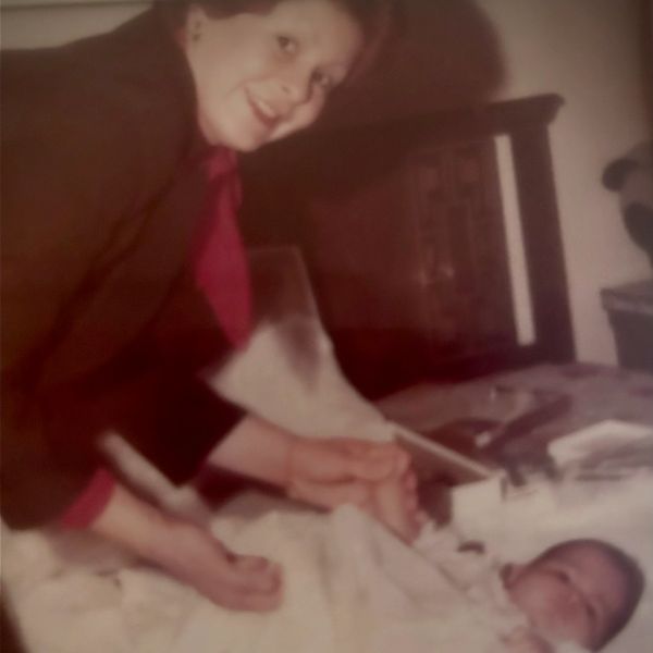 A woman smiling while caring for a baby lying on a bed.