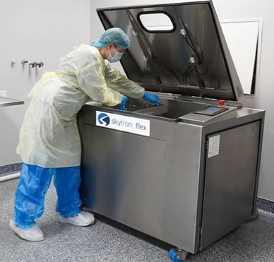 Healthcare worker in protective gear operating a sterilization machine.