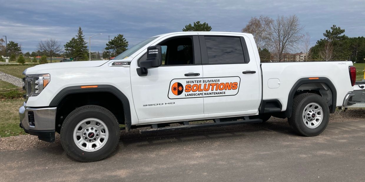 White truck with Winter Summer Solutions landscape maintenance logo.