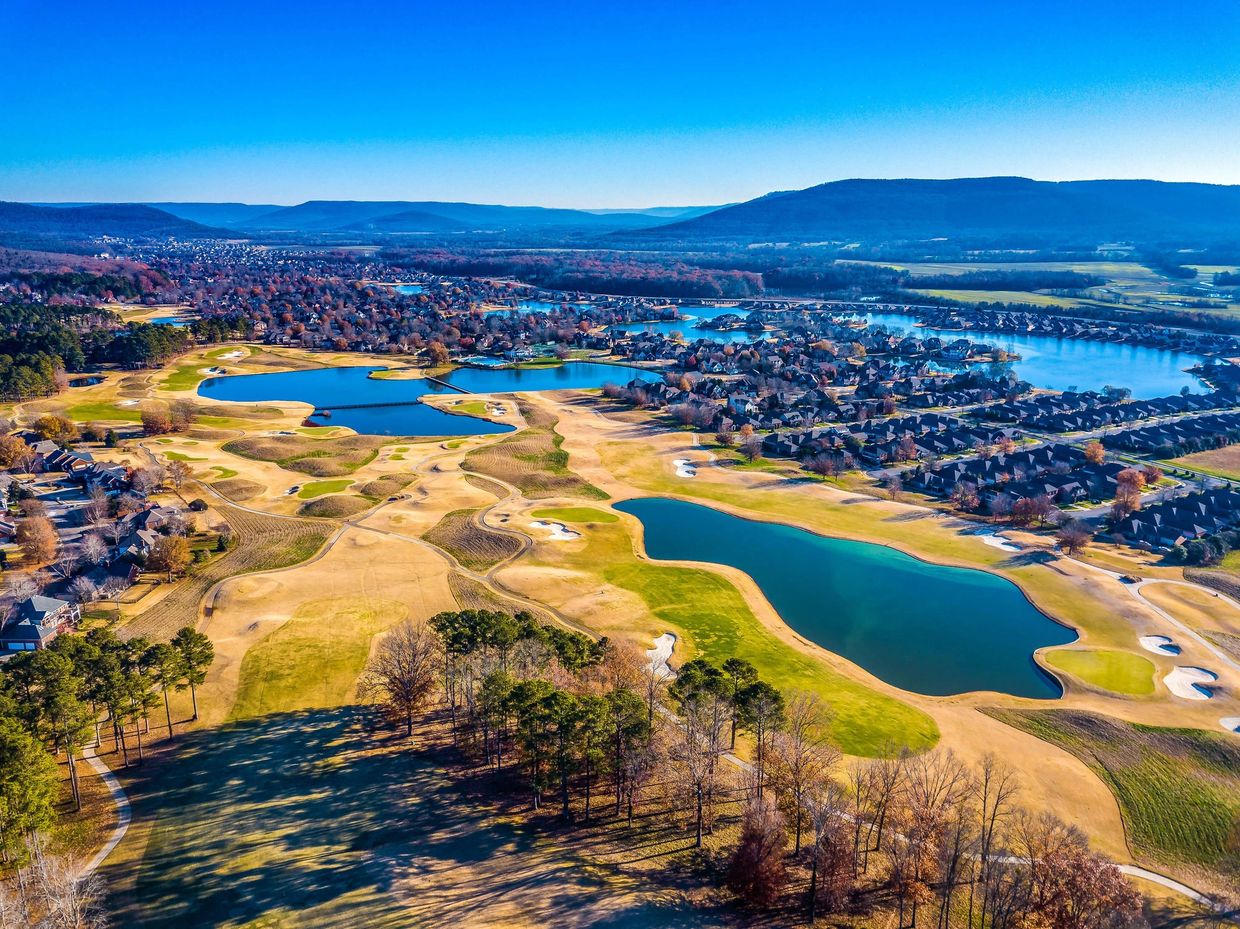 Aerial view of a golf course with lakes and nearby residential area under clear blue sky.