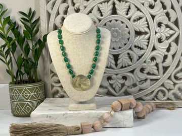 Green bead necklace with a large gold pendant displayed on a stand.