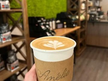 Hand holding a latte with latte art in a cozy coffee shop.