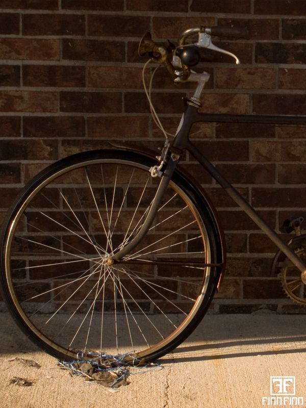 Old bicycle with a flat front tire locked to a brick wall.