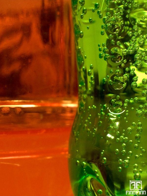 Close-up of bubbles in a green carbonated bottle with an orange background.