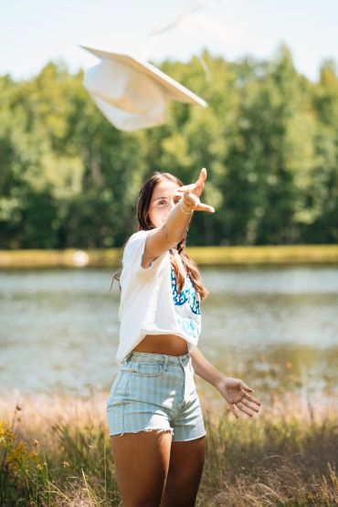 Young woman throws a graduation cap outdoors by a lake.