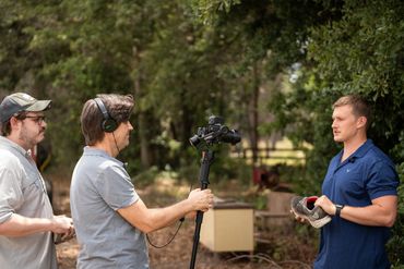A man in blue scrubs holding a turtle, being filmed outdoors.