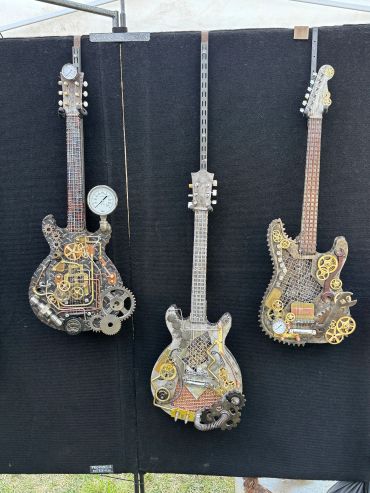 Three steampunk-style guitars mounted on a black board.