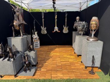 Outdoor display of sculptures and guitars under a tent.