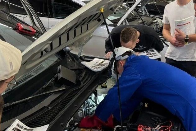 People inspecting a car engine with manuals.