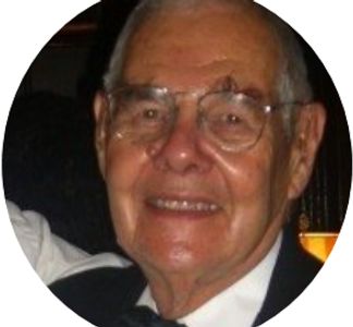 Elderly man smiling, wearing glasses and a tuxedo.