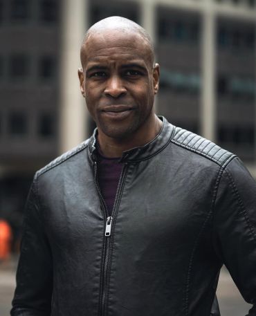 Man wearing a black leather jacket smiles gently.