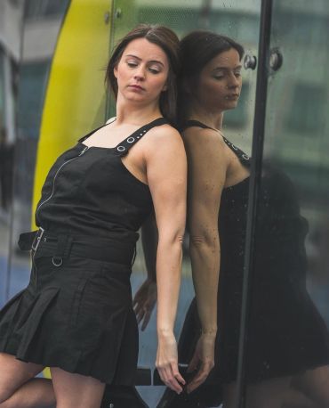 Woman in black outfit leaning against a reflective glass wall.
