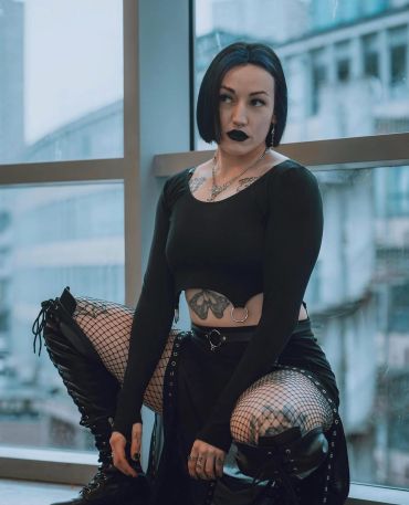 Woman in goth-inspired outfit with dark lipstick and fishnet stockings.