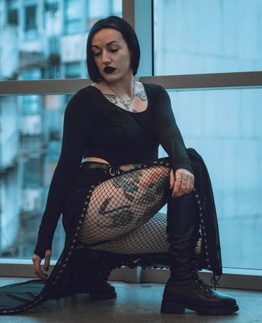 Woman in gothic outfit with tattoos and fishnet stockings.