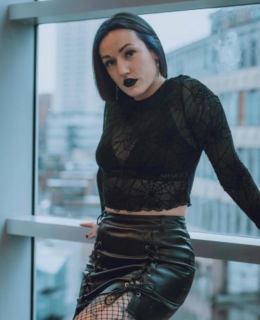 Woman in goth-inspired black outfit by a window.