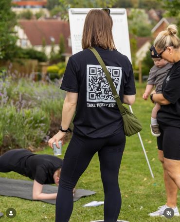 Person in black shirt with QR code on back outdoors.