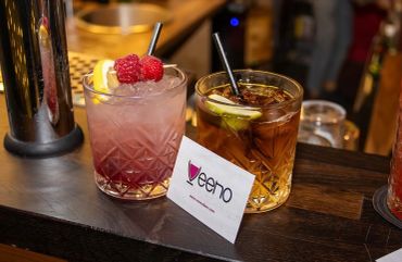Two cocktails on a bar counter with a business card.