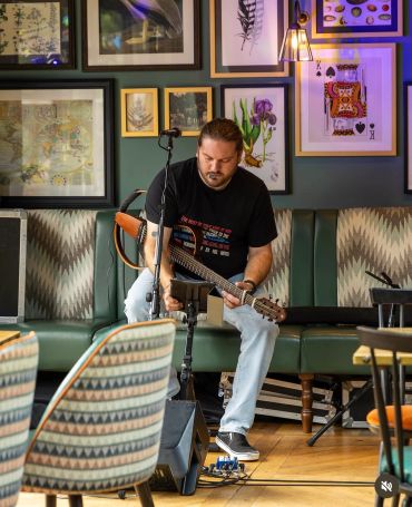 Man playing guitar in a cozy cafe with framed art.