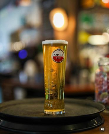 A tall glass of Amstel beer on a tray.