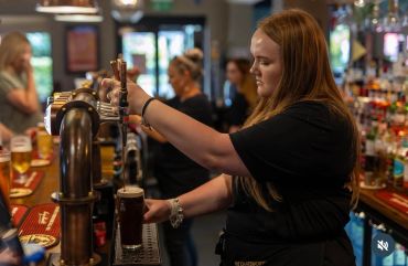 Bartender pouring a draft beer at a busy bar.