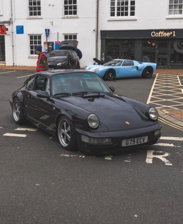 Black Porsche parked with a blue sports car in the background.
