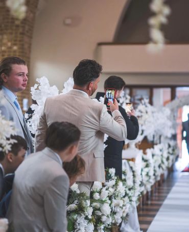 Men in suits at a decorated wedding aisle, one taking a photo.