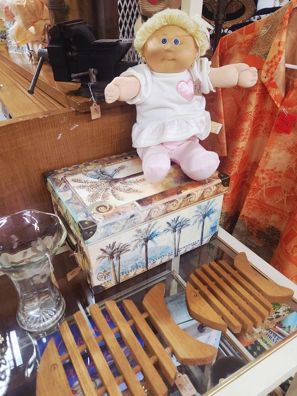 Vintage Cabbage Patch doll sitting on a decorative box among wooden items.