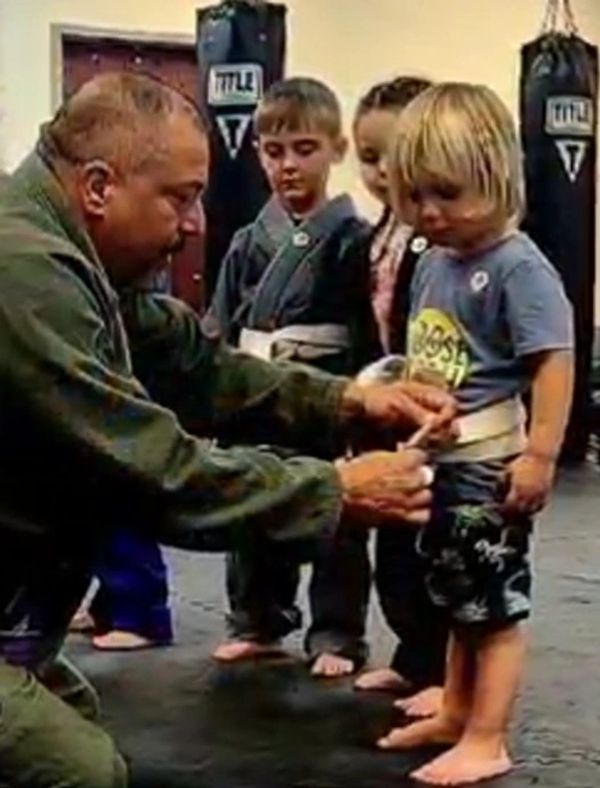 Martial arts instructor tying belt on young child in class.